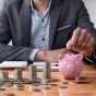 Businessman,Saving,Money,With,Piggy,Bank,And,Coins,On,Desk,