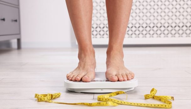 Woman,Standing,On,Floor,Scale,And,Measuring,Tape,At,Home,