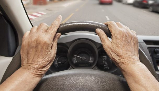 Senior,Woman,Driving,A,Car,On,Street,In,City.